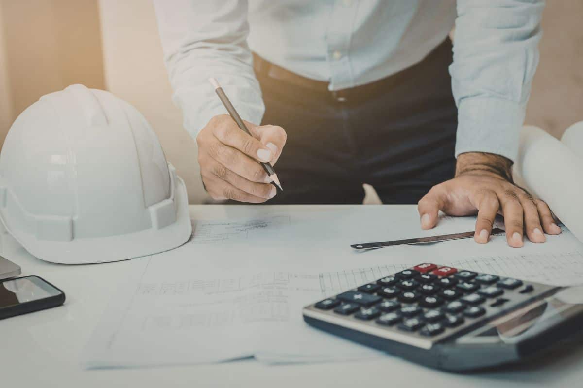 Lender calculating loan terms with a hard hat and plans on the desk